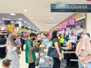Área de checkout de supermercado movimentada com vários clientes aguardando em filas longas nos caixas numerados, ilustrando congestionamento e o risco de abandono de filas em ambiente varejista. Busy supermarket checkout area with multiple customers waiting in long lines at numbered checkout counters, illustrating the risk of queue abandonment in a retail environment